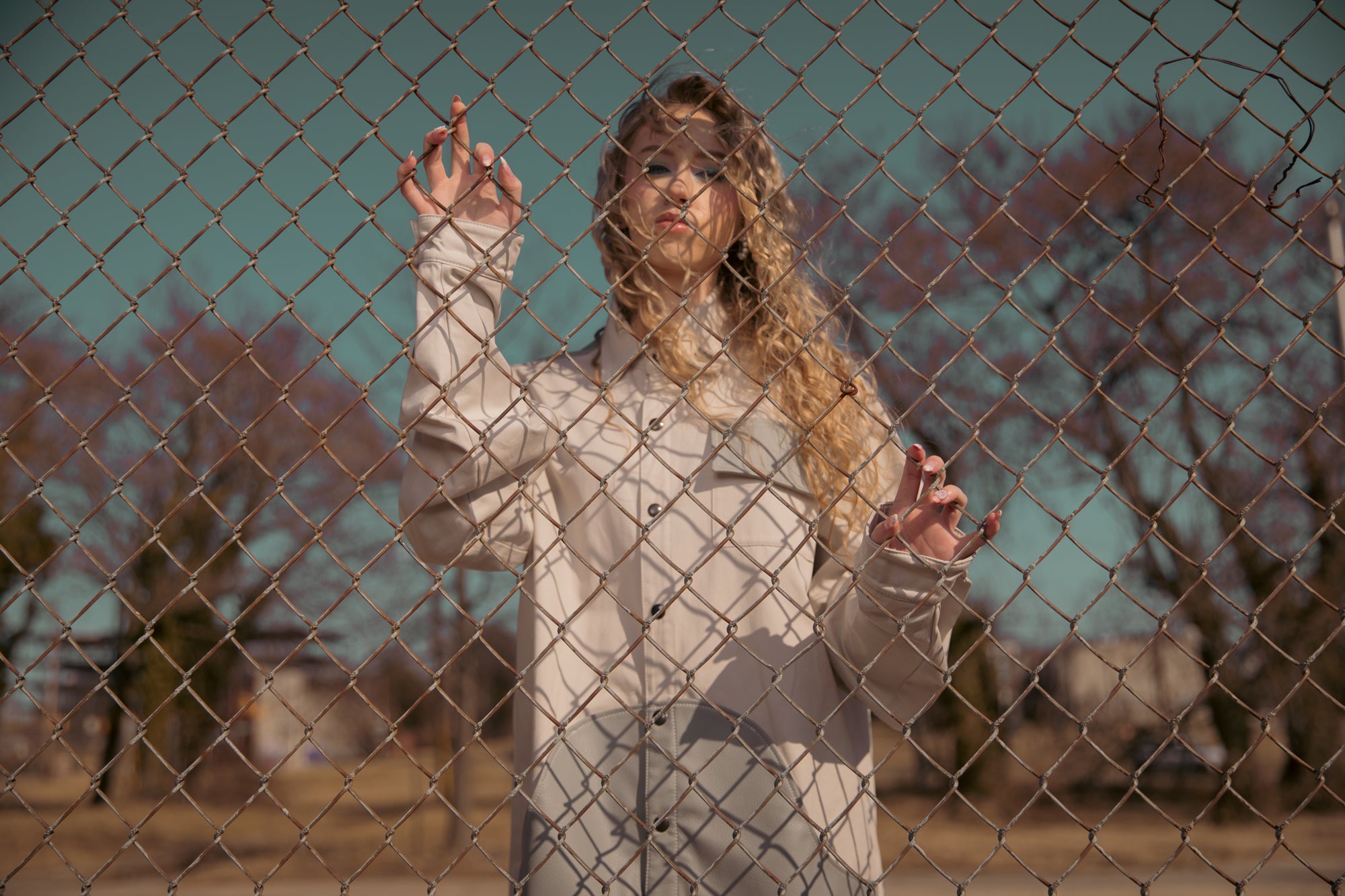 Light colored button-up shirt worn behind chain-link fence, minimal outdoor setting with soft light and shadows