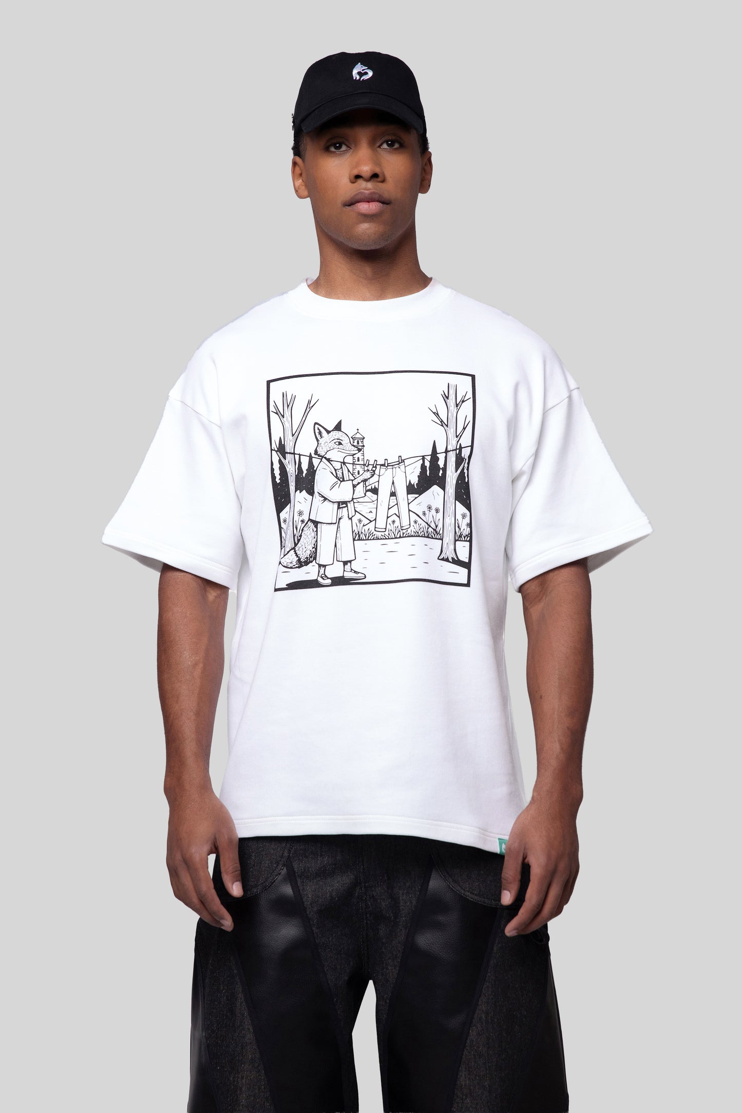 Model wearing white Supima cotton Lineage Tee with black graphic and black cap, front view