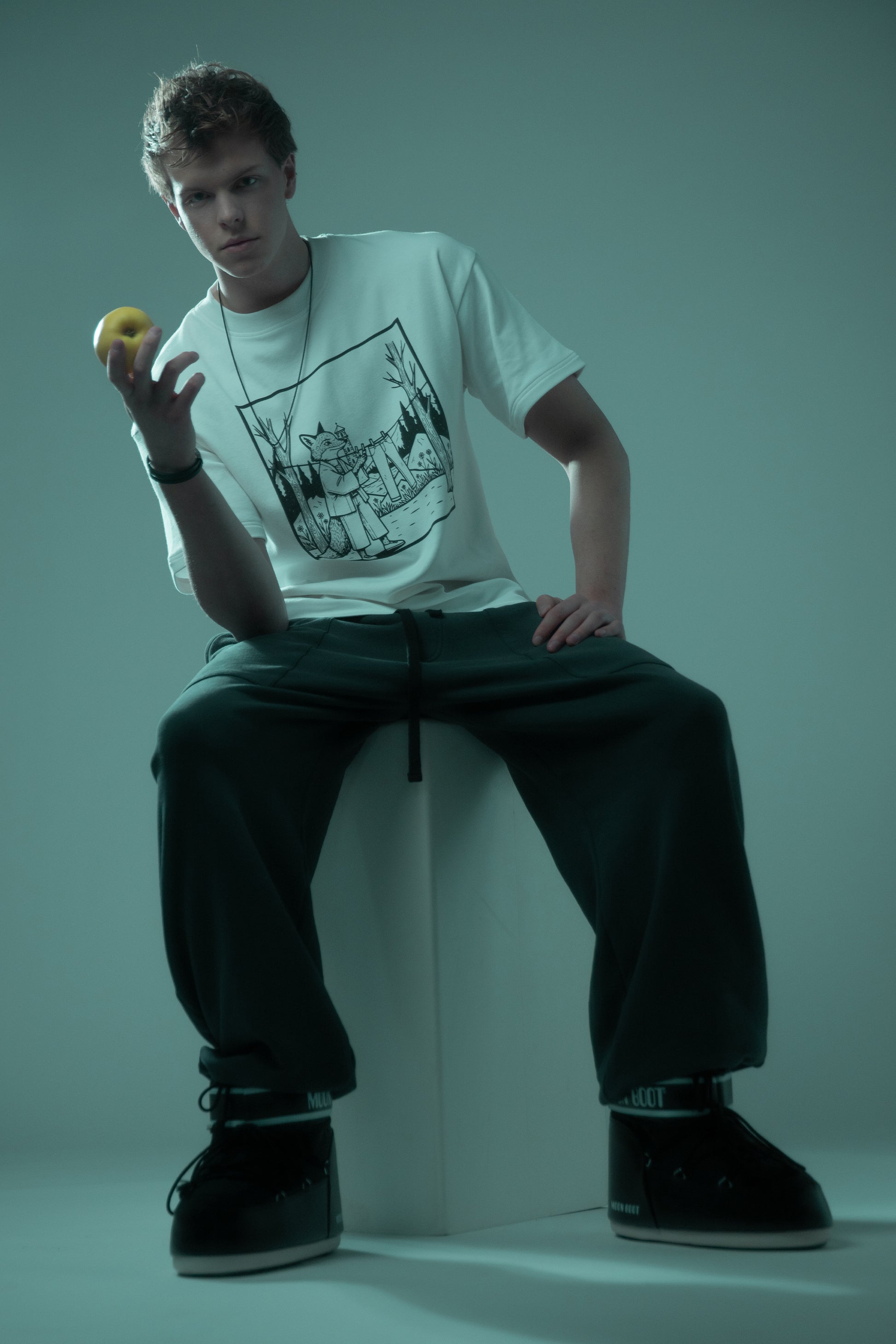 Model seated wearing white Supima cotton Lineage Tee with black DTG graphic, full look