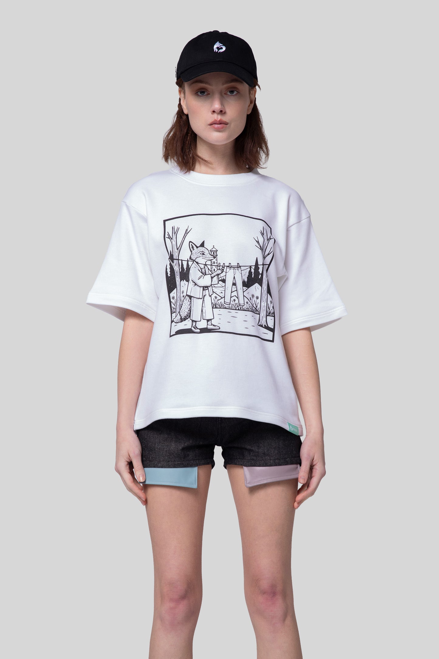 Model wearing white Supima cotton Women’s Lineage Tee with black fox graphic and black cap